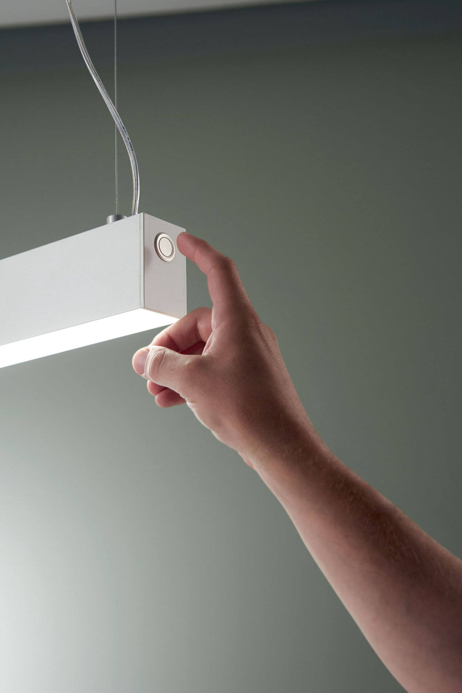 Main actionnant le bouton tactile situé à l'extrémité du luminaire blanc