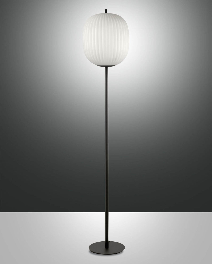 Lampadaire noir sur fond gris dégradé, abat-jour ovale blanc plissé allumé