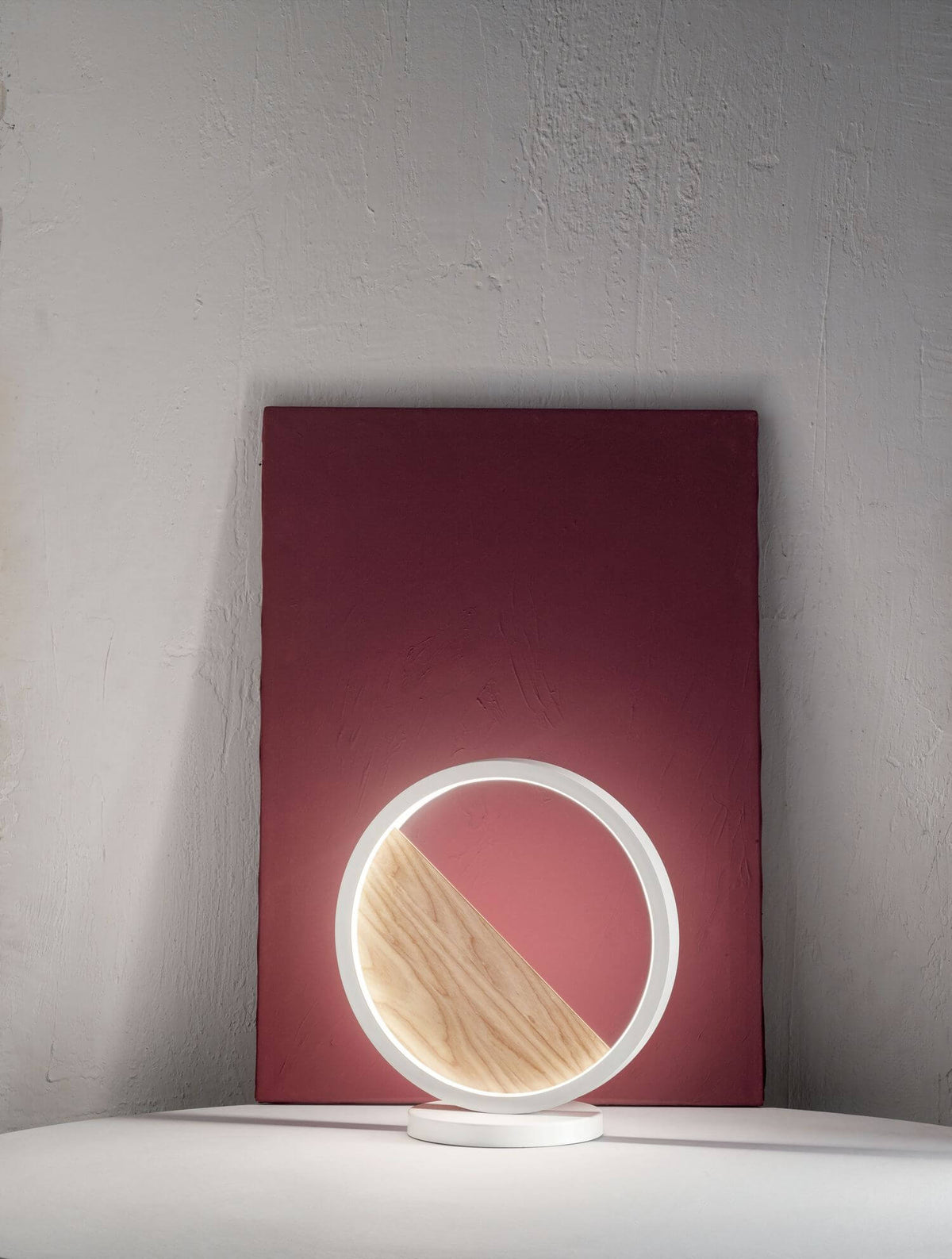 Mise en ambiance de la lampe ronde posée devant un panneau rouge et un mur brut