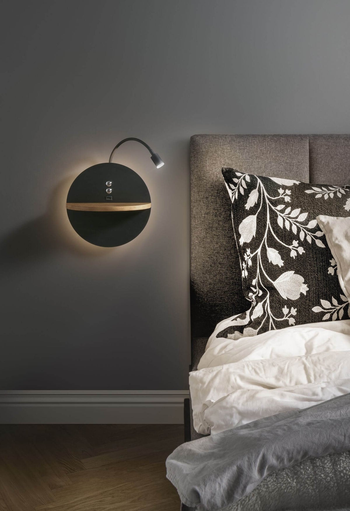 Mise en ambiance dans une chambre, applique murale noire allumée avec halo et bras de lecture.