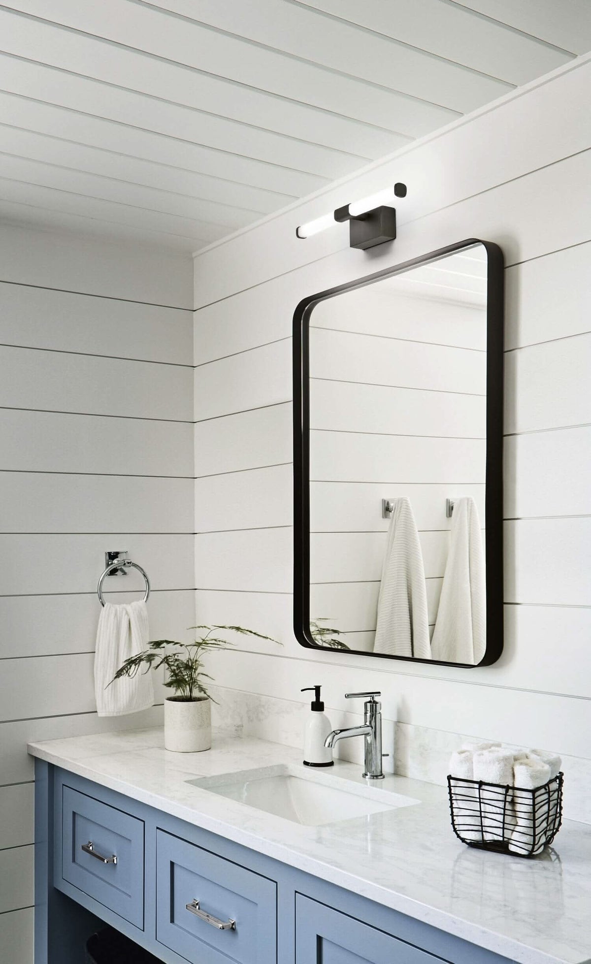 Mise en ambiance au-dessus d'un miroir de salle de bain, murs lambris blancs et vasque bleue.