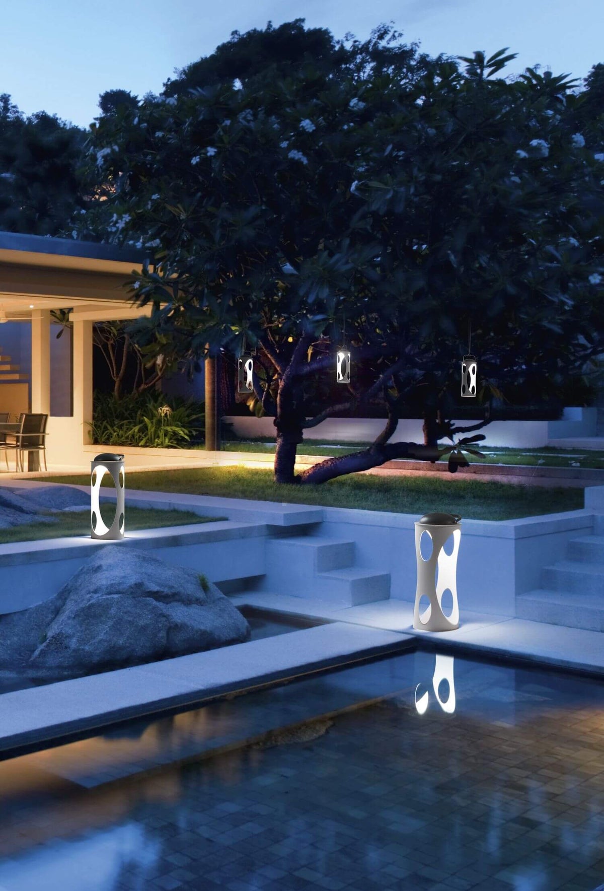 Mise en ambiance nocturne : lampes suspendues et posées autour d’une piscine.