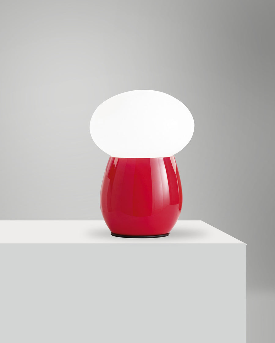 Lampe rouge présentée de loin sur un socle blanc, éclairage diffus