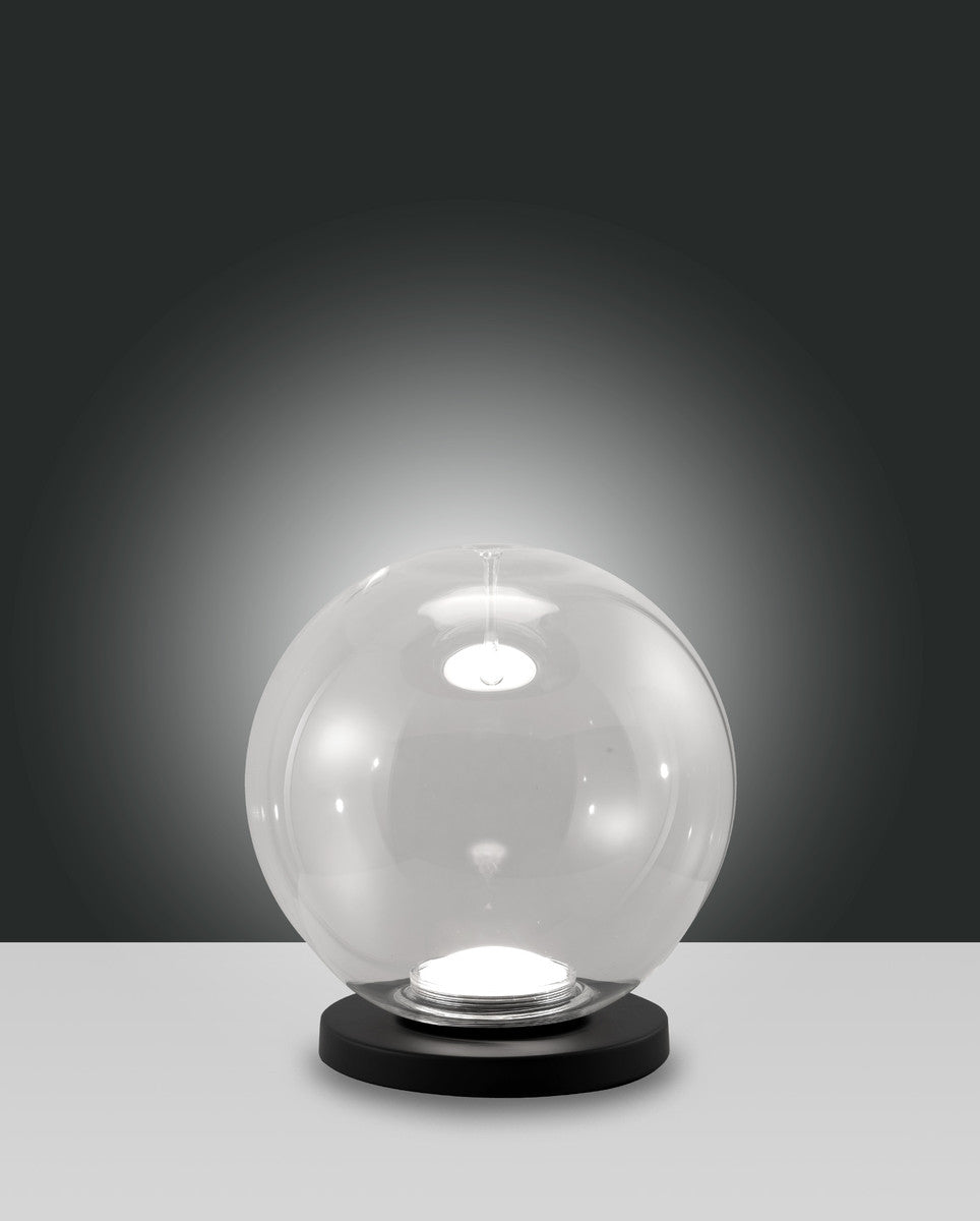 Lampe à poser boule en verre transparent sur socle rond noir, fond gris dégradé