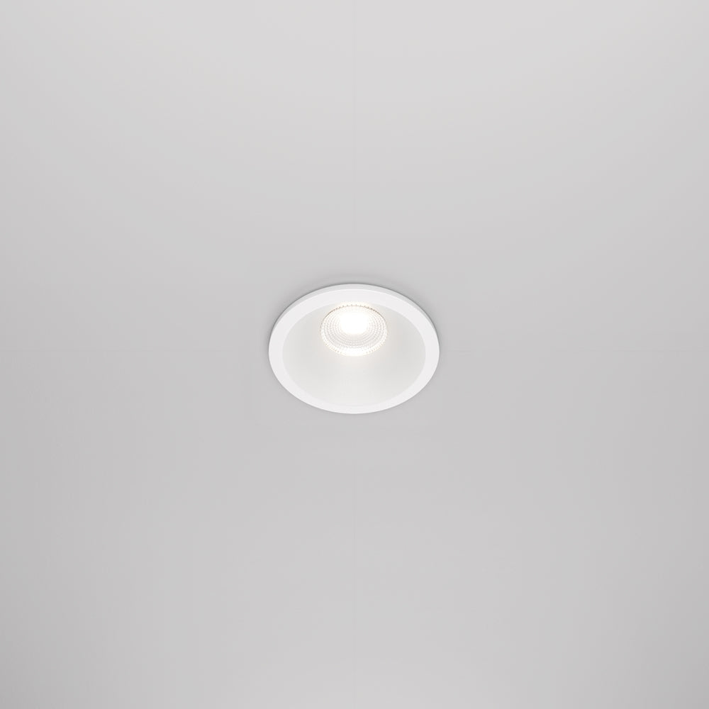 Vue de face d'un spot encastré blanc rond allumé dans un plafond.