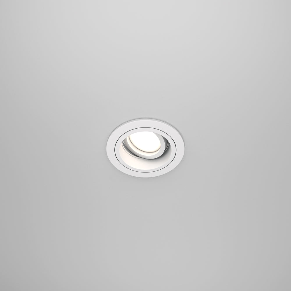 Spot encastré rond blanc vu de face sur un plafond gris clair uni