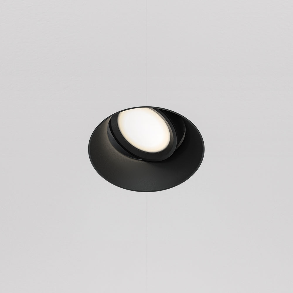 Spot encastré rond noir orientable allumé, vu de face sur plafond blanc
