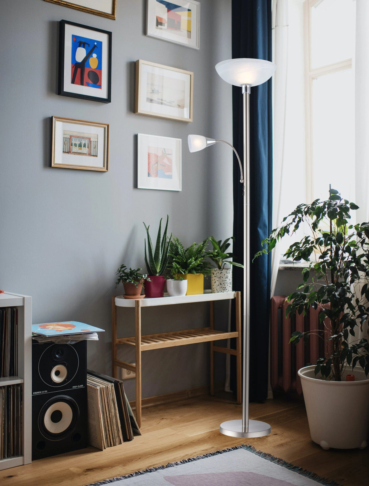 Mise en ambiance dans un salon, lampadaire allumé près d'une plante et de cadres