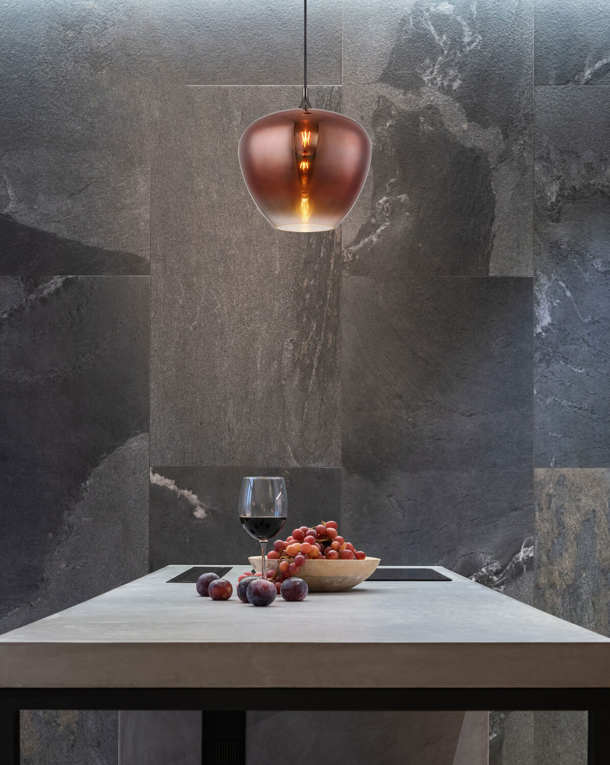 Suspension allumée au-dessus d'une table en pierre avec raisins et verre de vin.