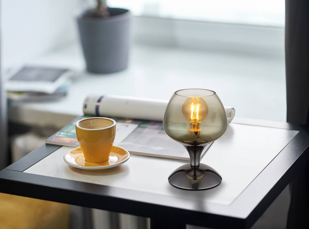 Lampe à poser allumée sur une table près d'une tasse jaune, ambiance intérieure