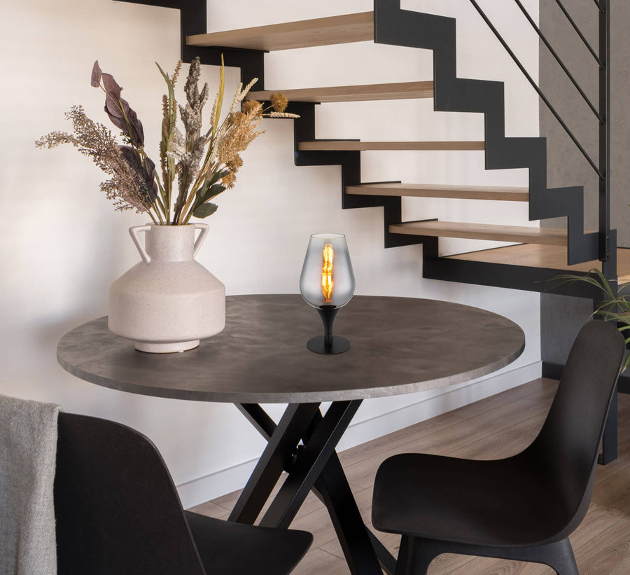 Lampe à poser noire sur table ronde en intérieur moderne, avec vase et escalier.