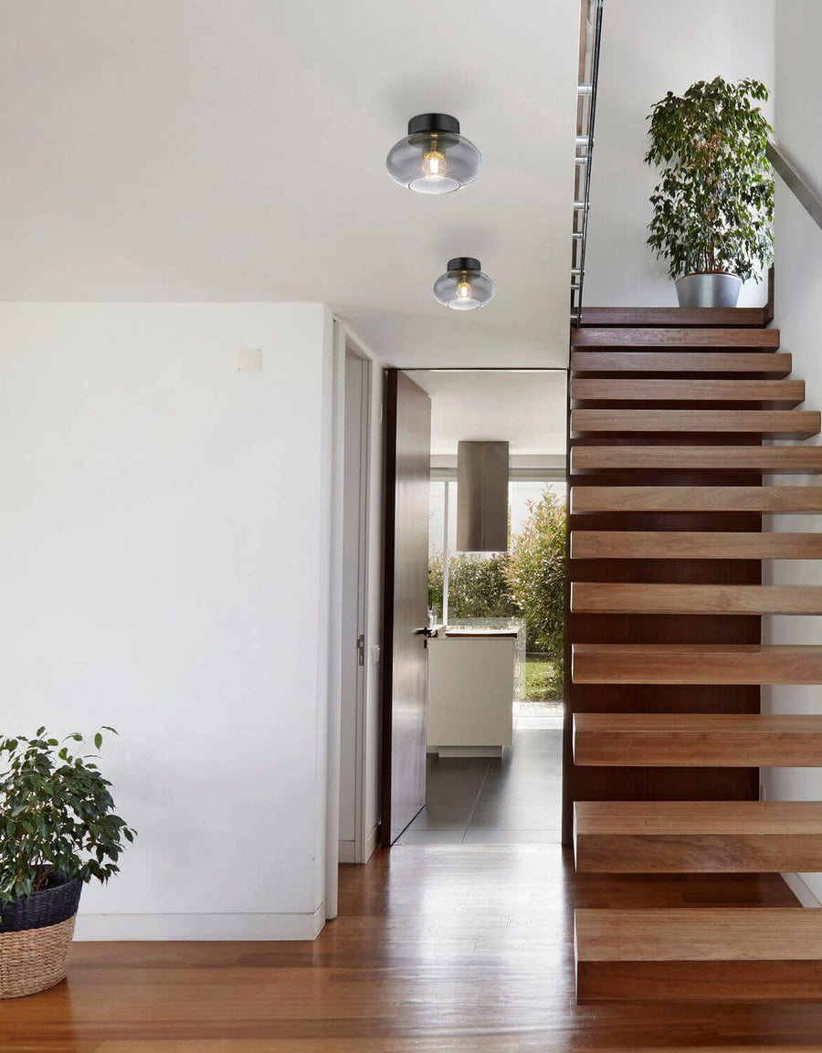 Deux plafonniers ronds éclairant un couloir moderne avec escalier en bois clair.