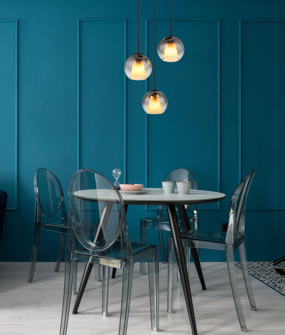 Mise en ambiance au-dessus d'une table à manger, suspension noire et globes fumés allumés.