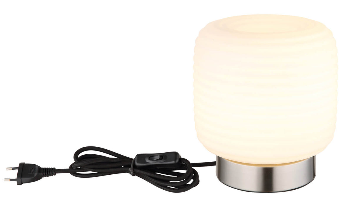 Lampe à poser allumée avec cordon noir, interrupteur et fiche électrique visibles sur fond blanc.