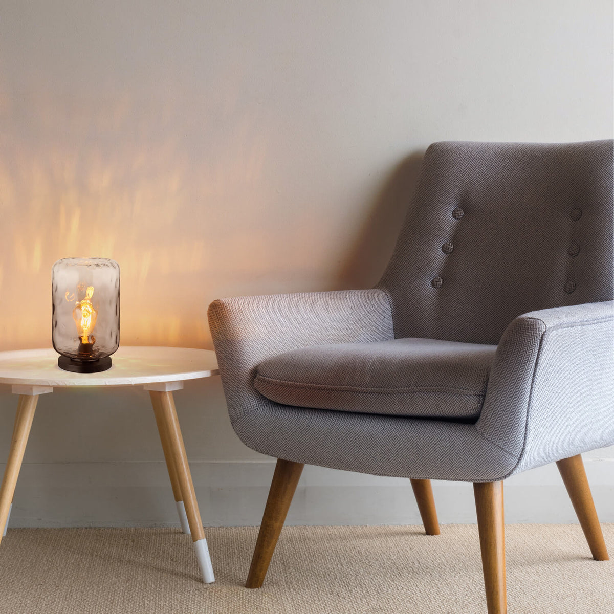 Mise en ambiance de la lampe posée sur une table basse près d'un fauteuil gris.