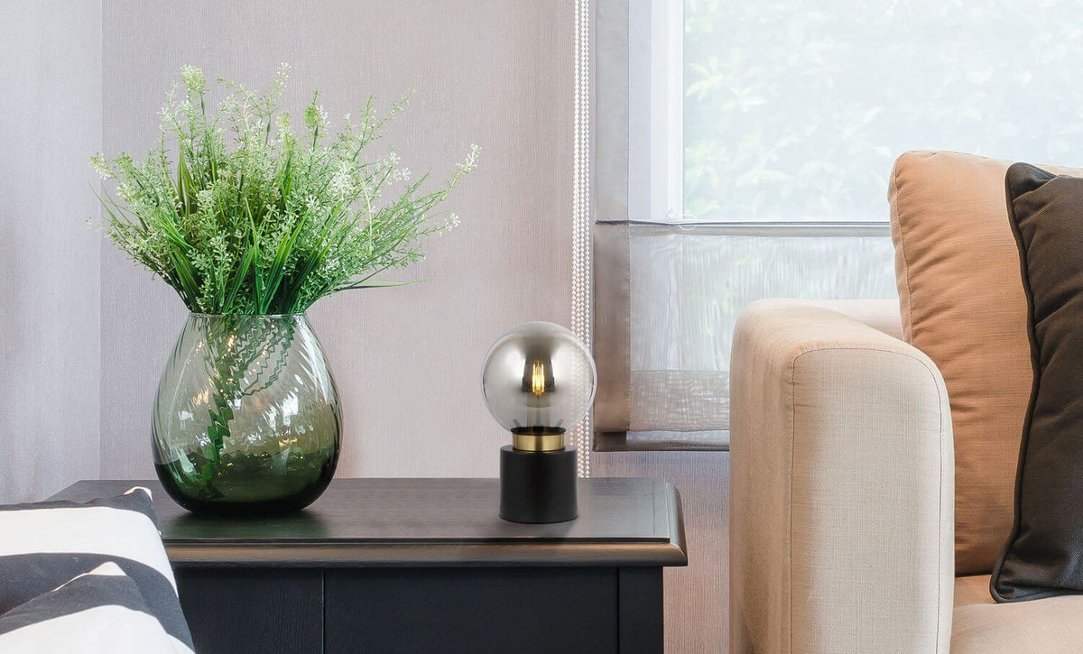Lampe posée sur un meuble noir près d'un vase de plantes, dans un salon.