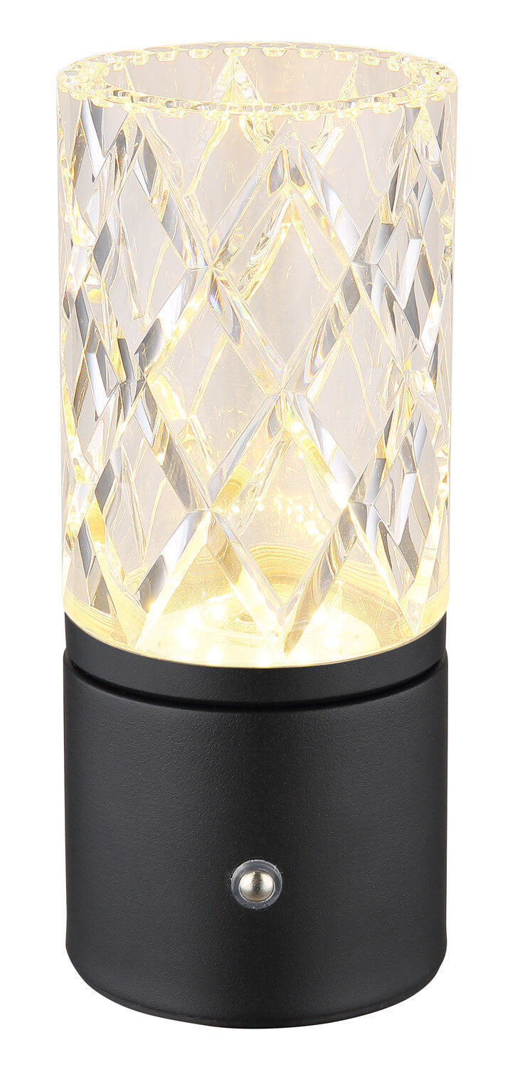 Gros plan de la lampe allumée, lumière chaude traversant l’abat-jour facetté, base cylindrique noire mate.