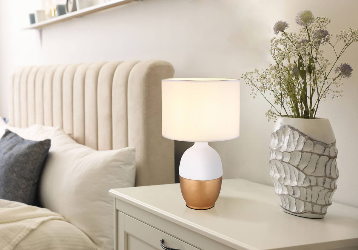 Mise en ambiance de la lampe posée sur une table de chevet, près d'un lit