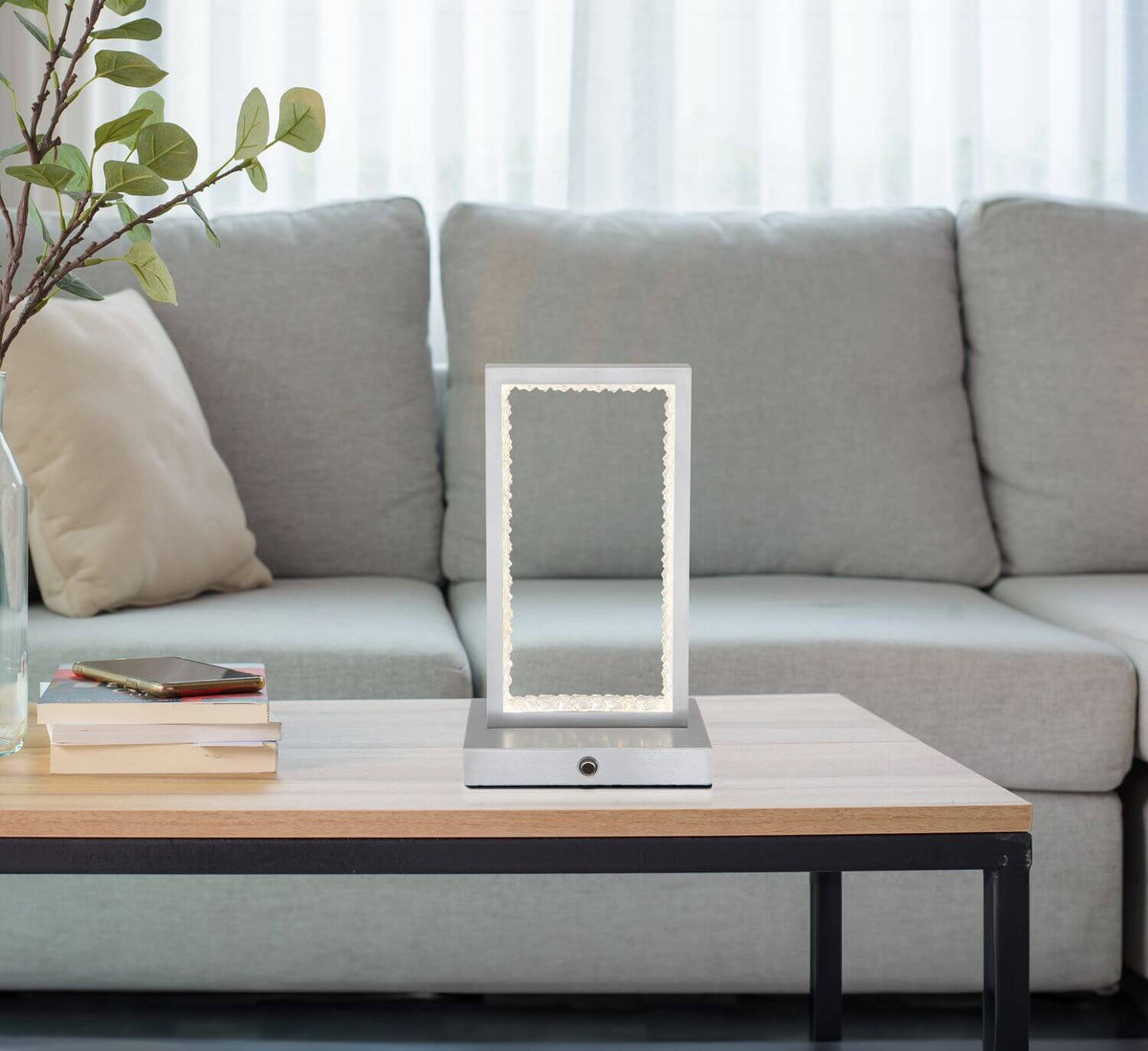 Mise en ambiance : lampe allumée sur table basse en bois devant un canapé gris