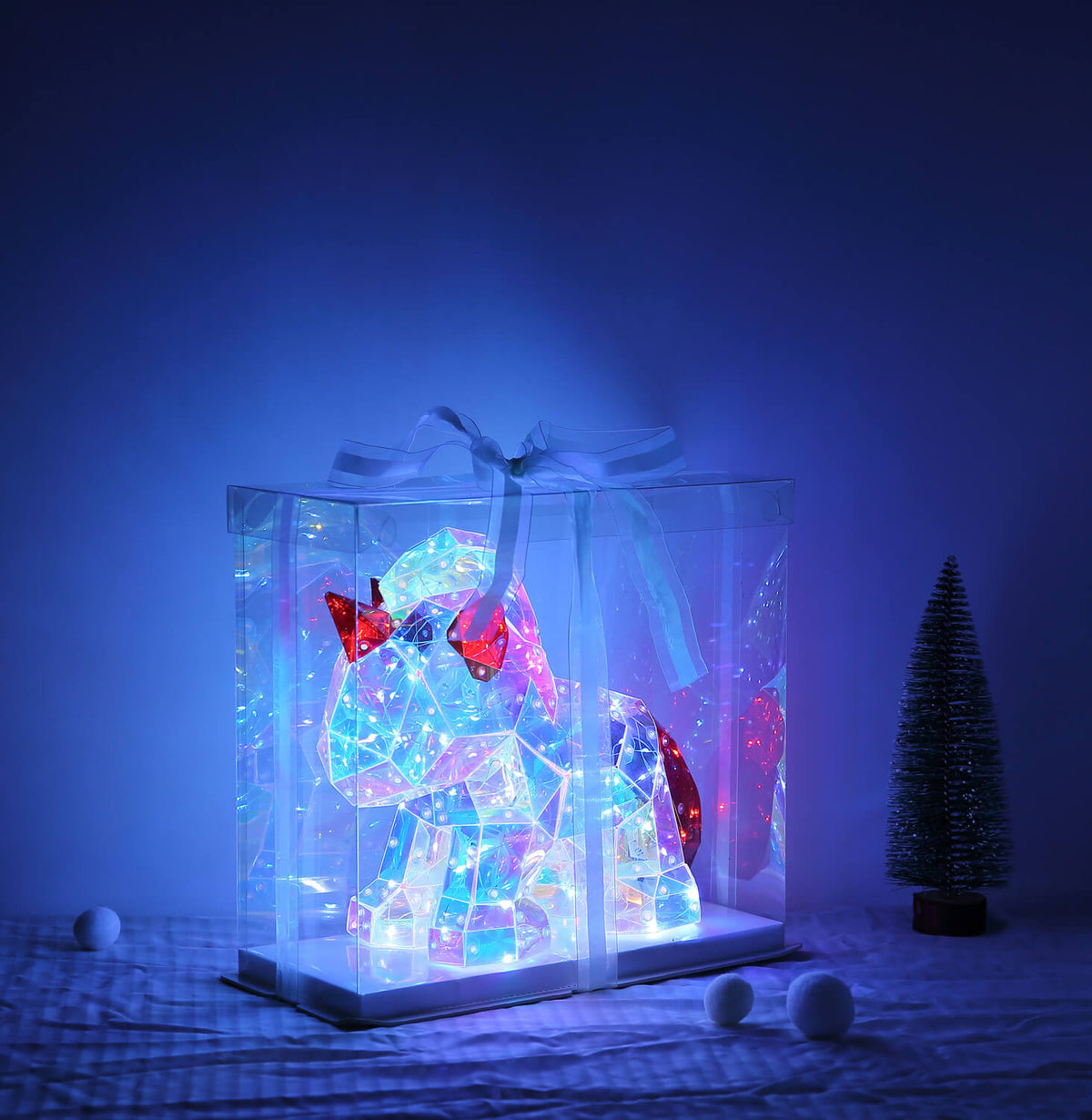 Mise en ambiance nocturne bleue, boîte lumineuse posée sur un lit, petit sapin.