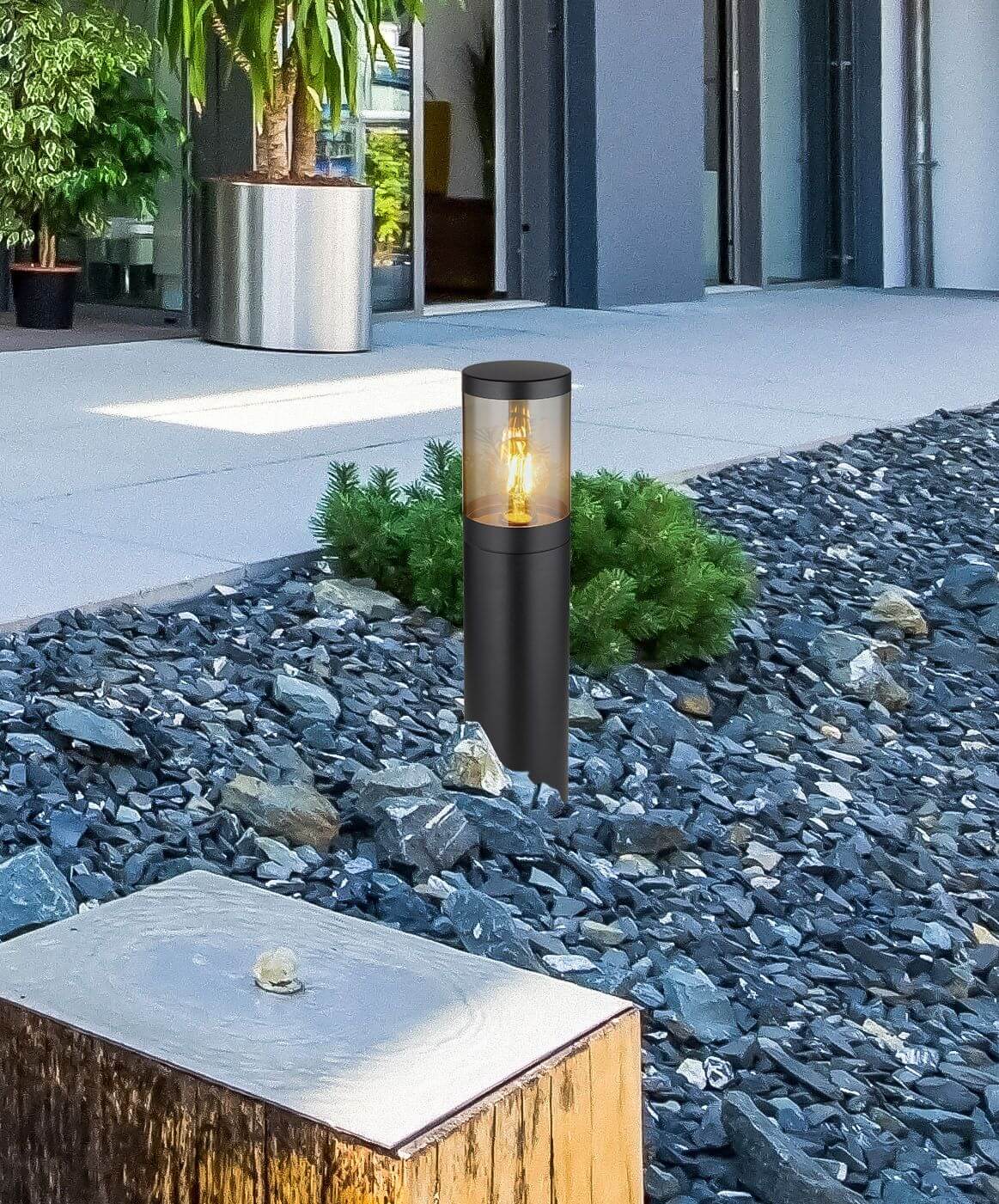 Mise en ambiance : luminaire éclairant une allée de gravier près de plantes et bâtiment moderne.