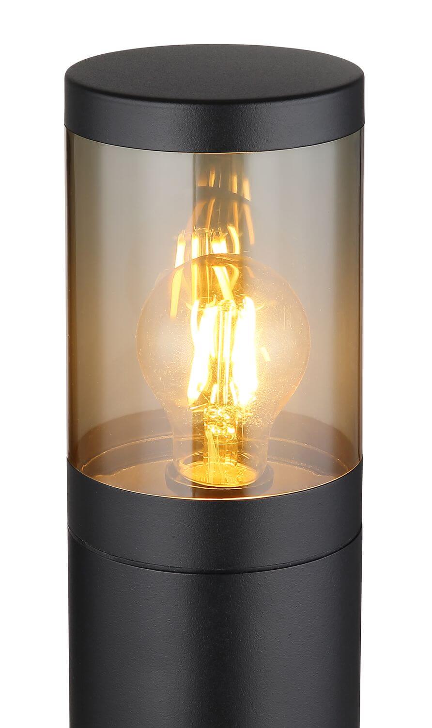 Détail rapproché du globe cylindrique ambré, ampoule filament allumée, capuchon et corps noirs mats.