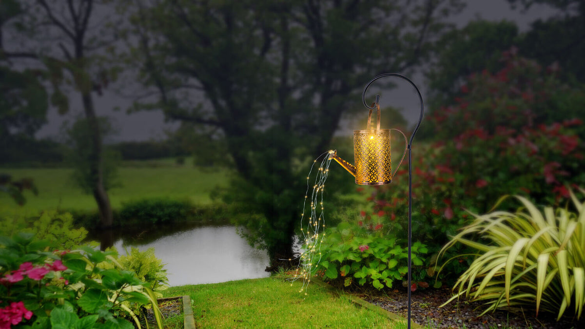 Mise en ambiance nocturne au jardin, arrosoir illuminé près d'un bassin et de fleurs