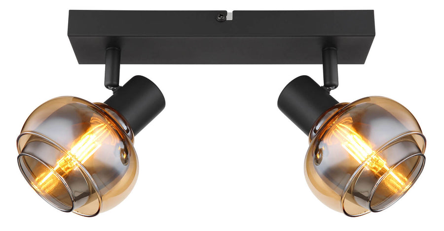 Gros plan du luminaire allumé, cadrant les deux verres ambrés et la base noire.