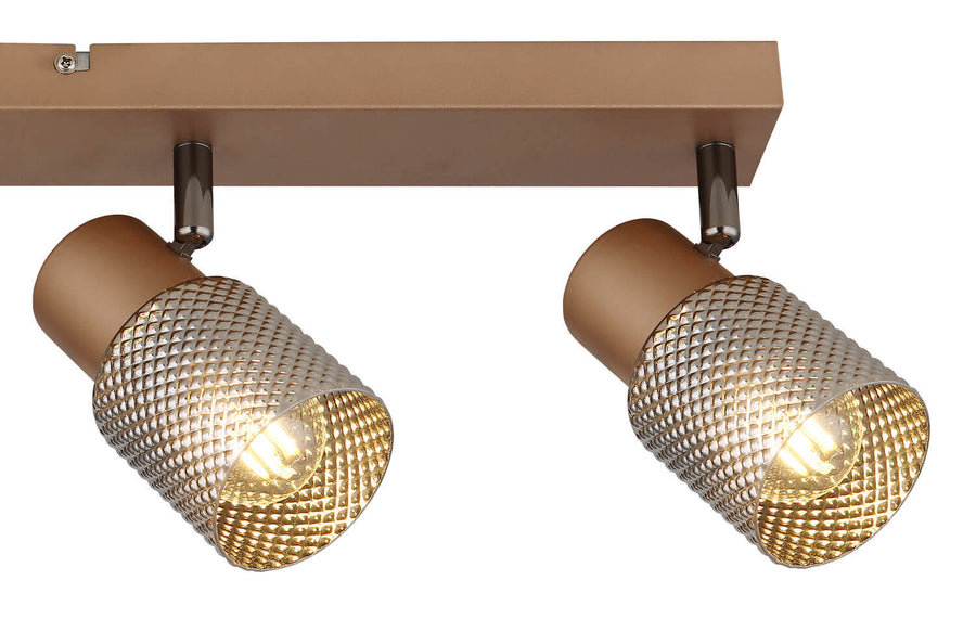 Gros plan sur deux spots orientables allumés et leur grille métallique perforée dorée.