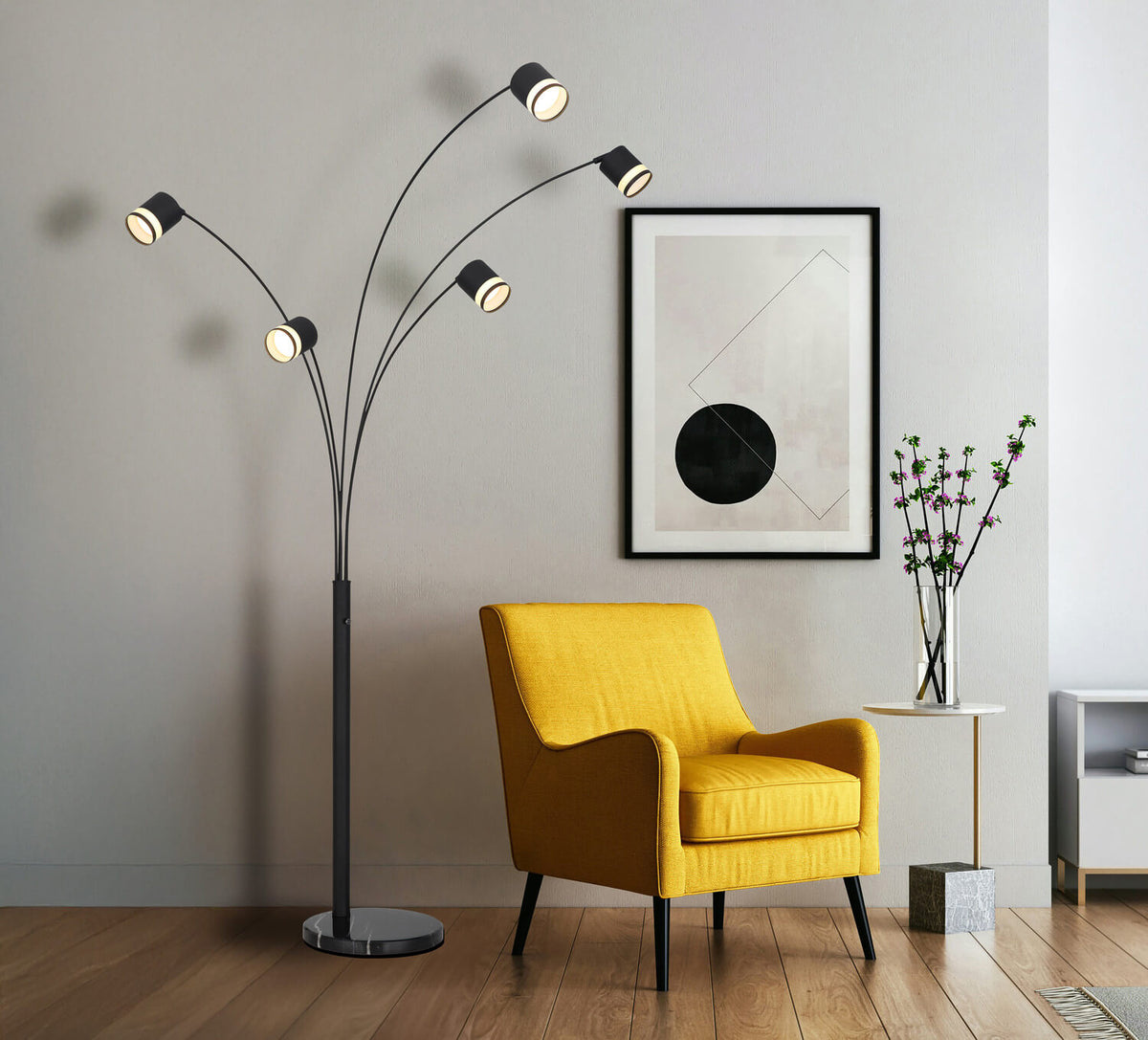 Mise en ambiance salon avec lampadaire noir, fauteuil jaune, tableau encadré et vase de fleurs.