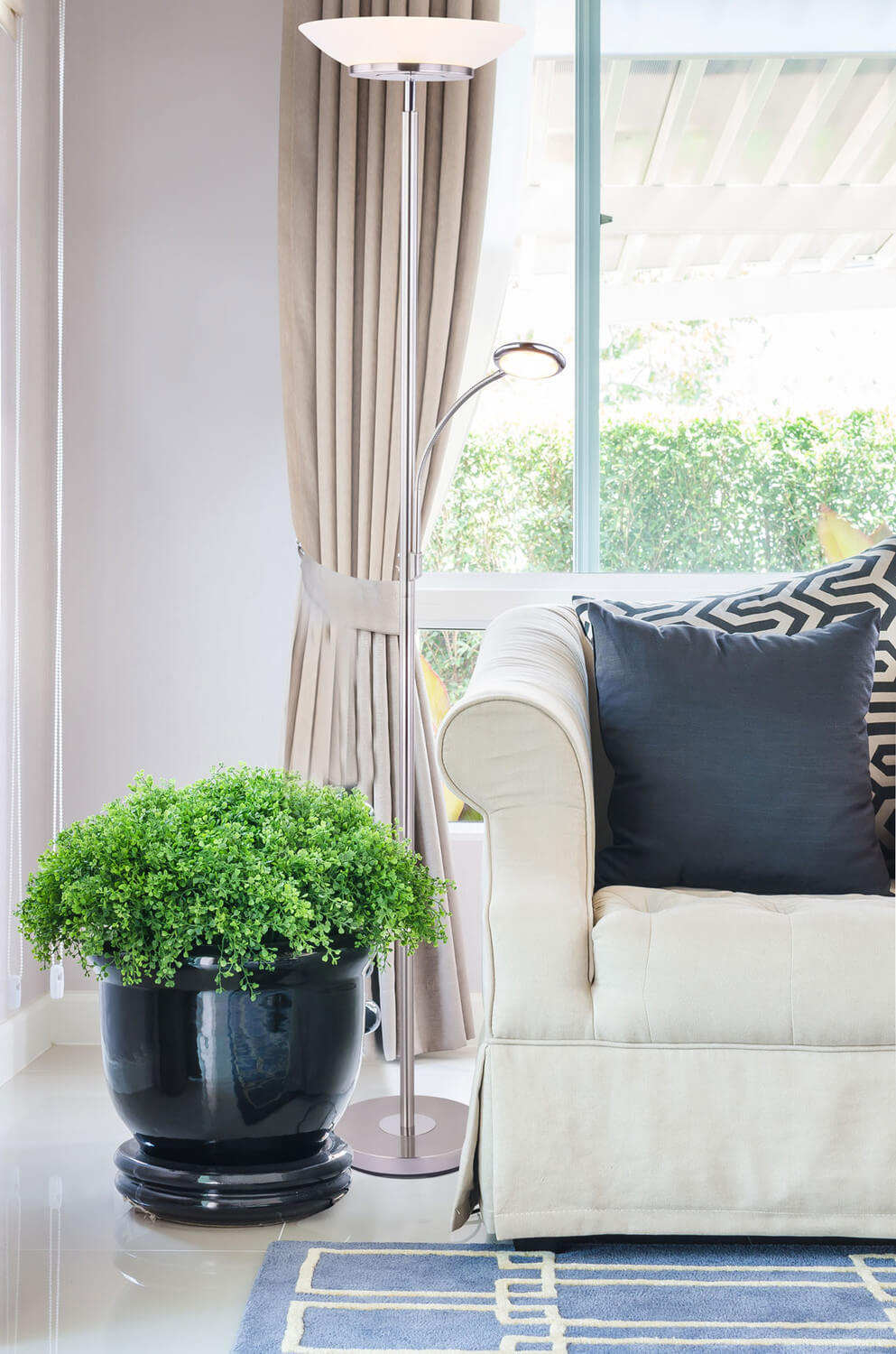 Lampadaire allumé placé devant la fenêtre, à côté du fauteuil beige