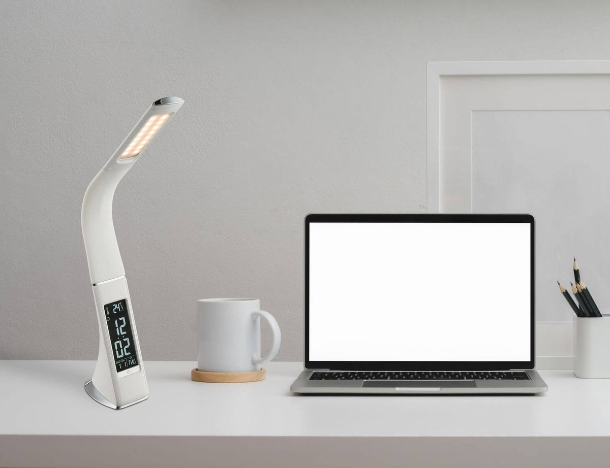 Lampe à poser blanche sur un bureau, près d'un ordinateur portable, d'une tasse et de crayons.