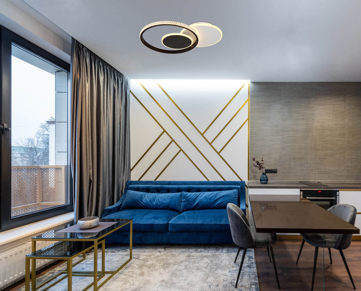 Mise en ambiance dans un salon moderne, plafonnier allumé au-dessus du canapé bleu.