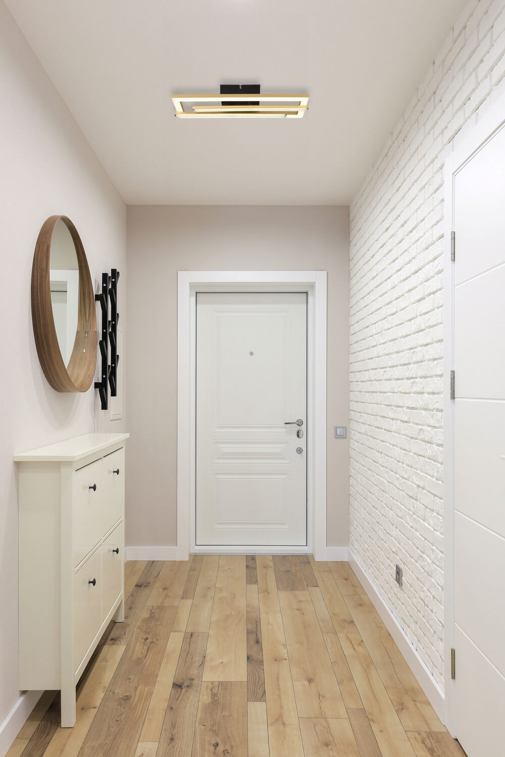 Mise en ambiance dans un couloir blanc avec commode et miroir rond