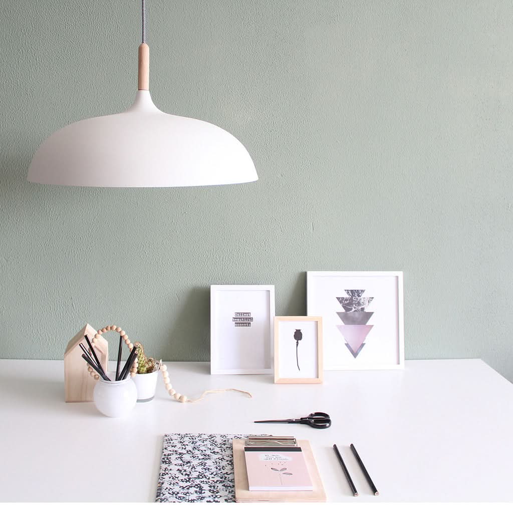 Luminaire allumé au-dessus d'un bureau blanc devant un mur vert sauge