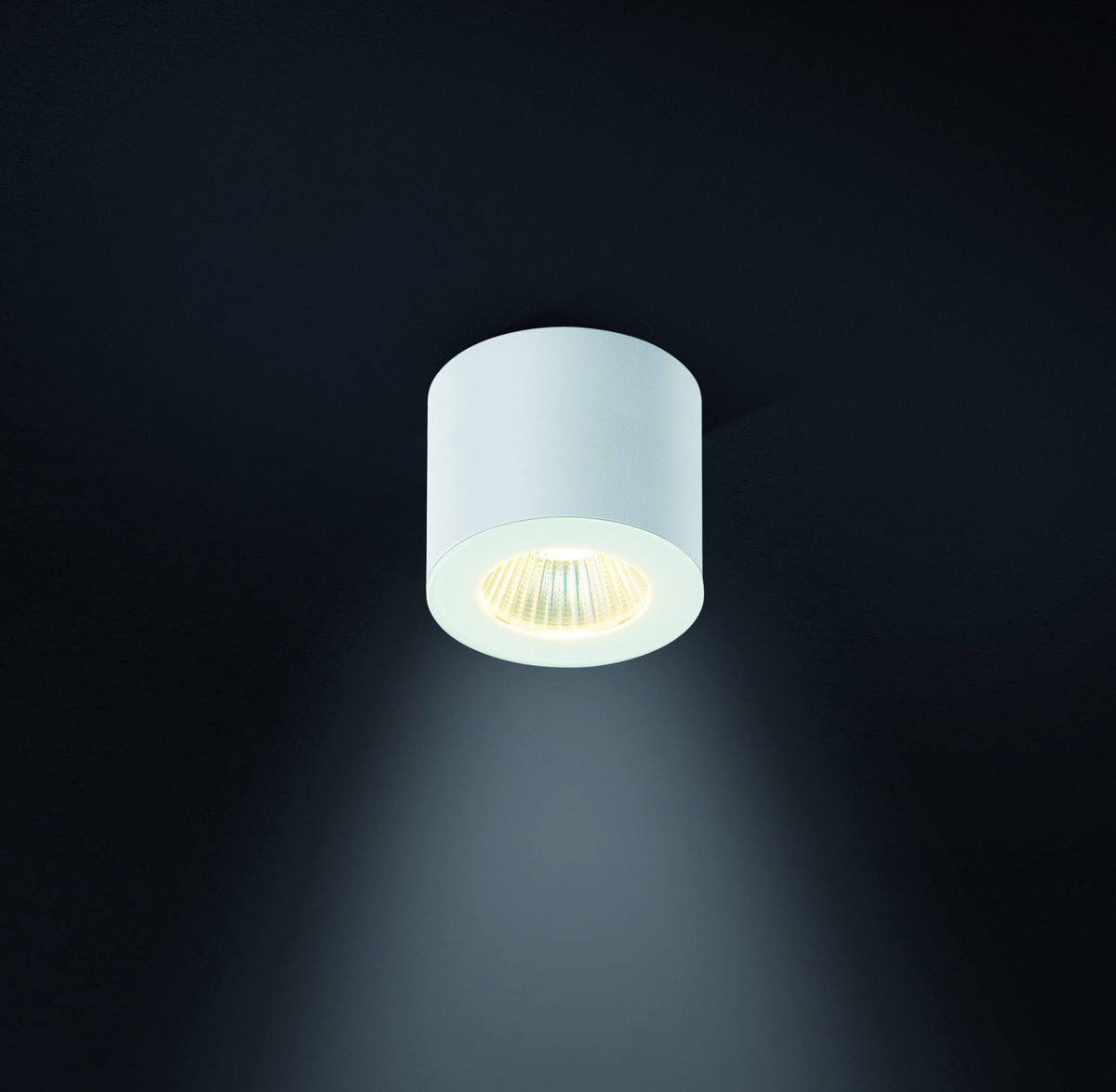 Plafonnier cylindrique blanc allumé sur fond sombre, mettant en valeur la lumière.