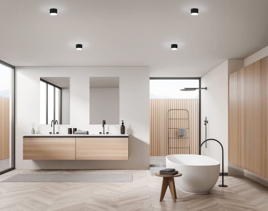 Vue large de la salle de bain en bois clair équipée des mêmes plafonniers cylindriques.