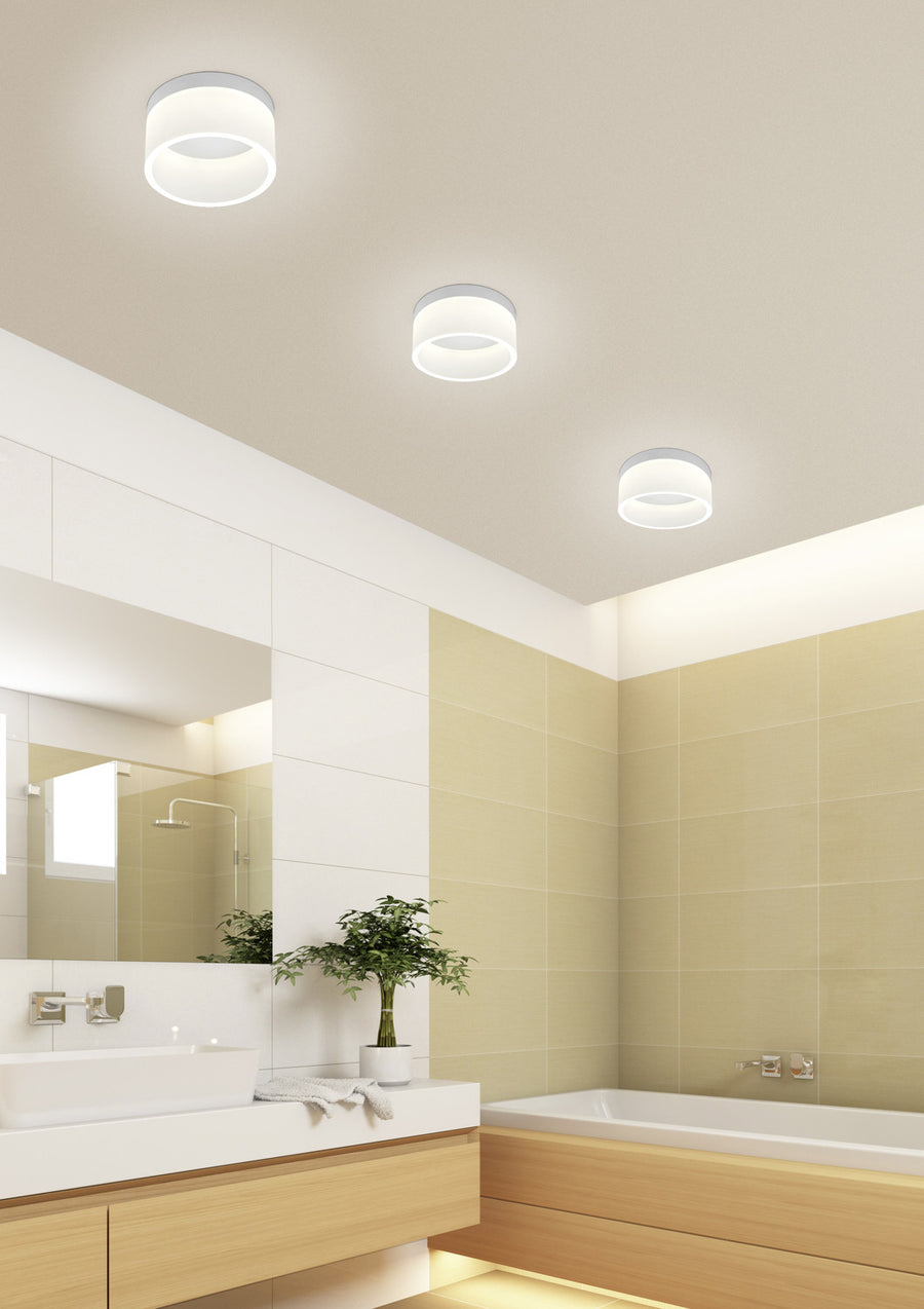 Trois plafonniers identiques allumés au plafond d'une salle de bain moderne claire.
