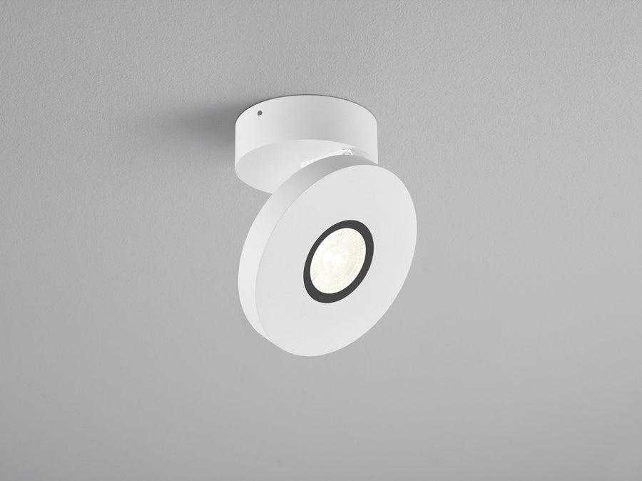 Plafonnier blanc orientable vu de trois quarts, projecteur rond sur fond gris clair