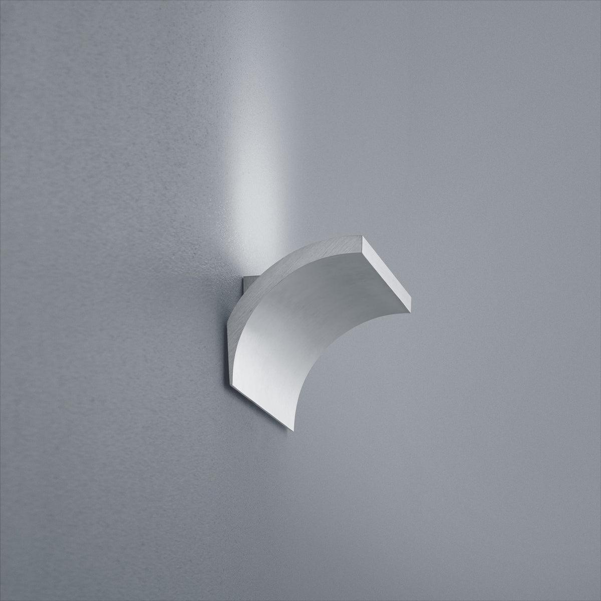 Vue de trois quarts de l'applique cintrée en métal nickelé fixée au mur gris