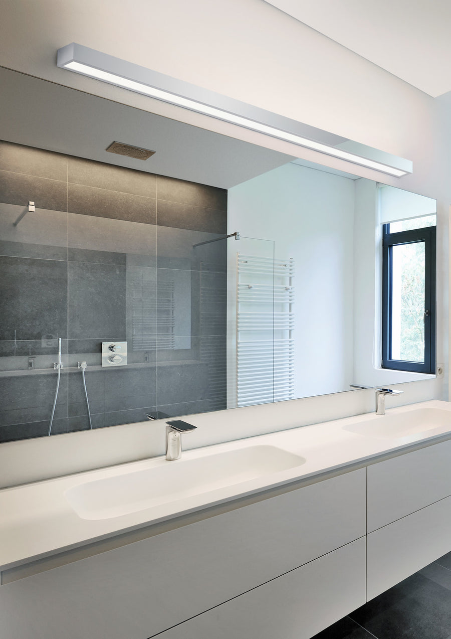 Luminaire allumé au-dessus d'un grand miroir de salle de bain claire