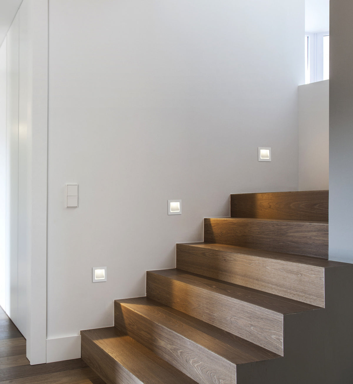 Mise en ambiance dans un escalier en bois, trois appliques murales éclairent les marches