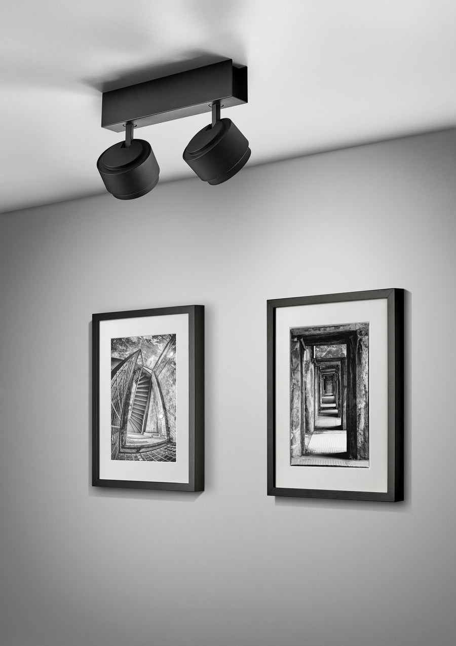 Version noire du plafonnier éclairant deux cadres photo accrochés au mur