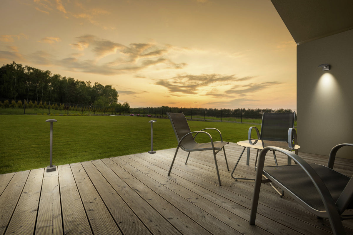 Mise en ambiance extérieure, applique allumée sur un mur près d'une terrasse en bois