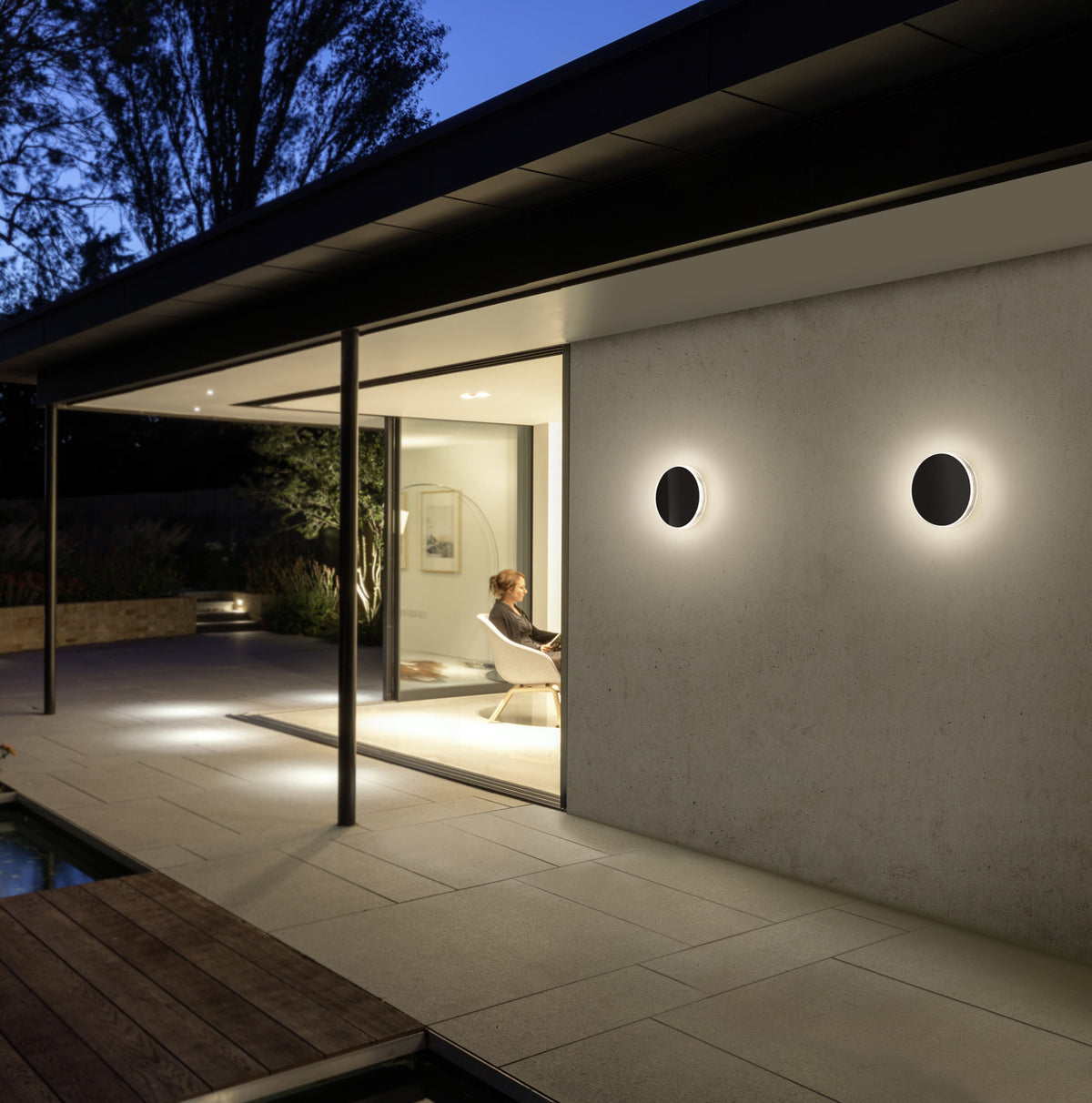 Mise en ambiance nocturne, deux appliques cerclées éclairant une terrasse en béton