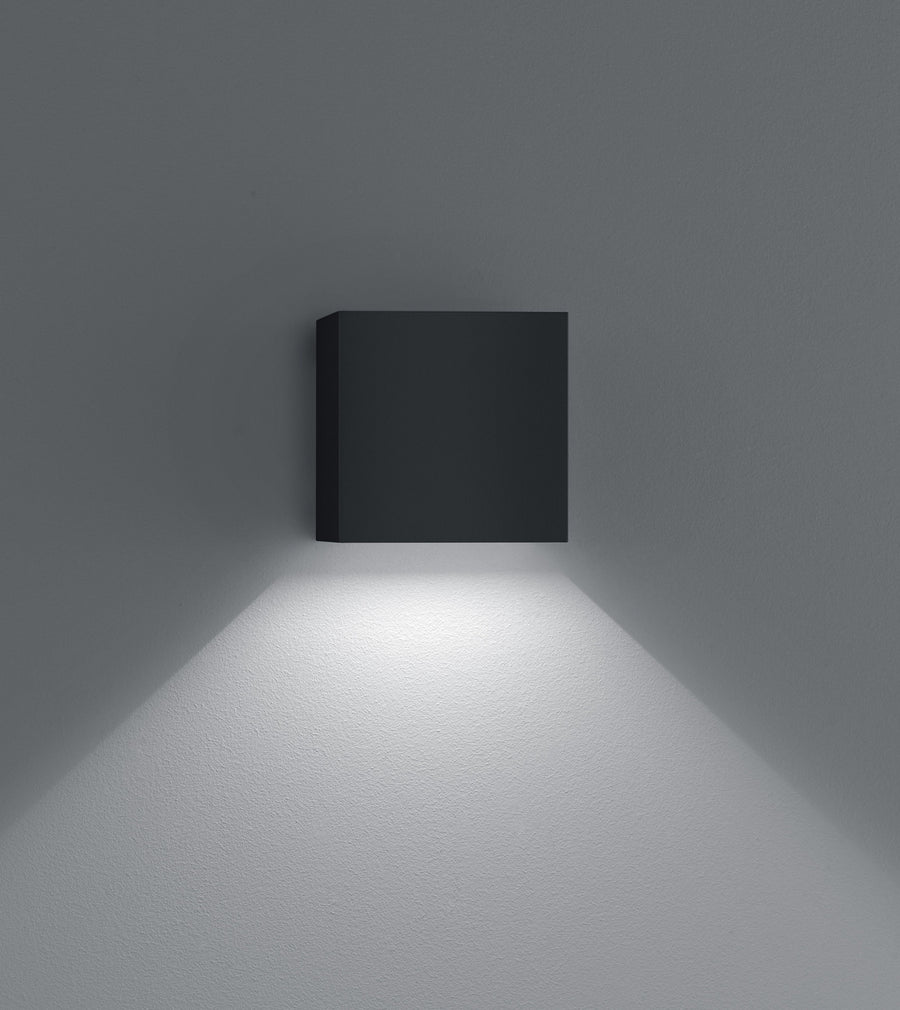 Vue de face du cube noir fixé au mur gris, halo lumineux vers le bas