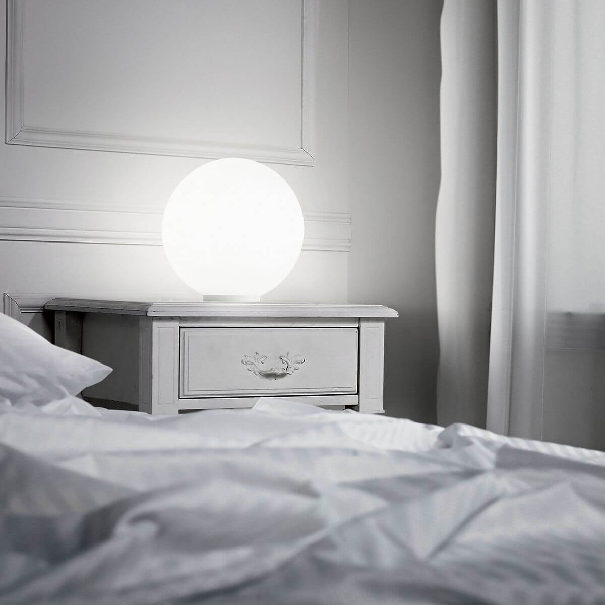 Lampe blanche allumée posée sur une table de nuit dans une chambre à coucher