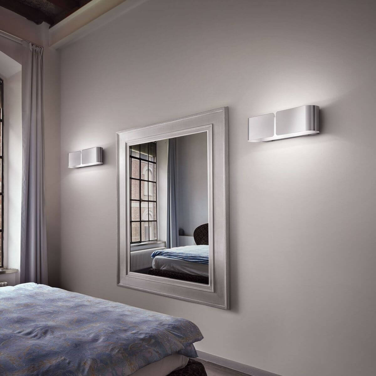 Mise en ambiance dans une chambre avec deux appliques murales chromées encadrant un miroir.