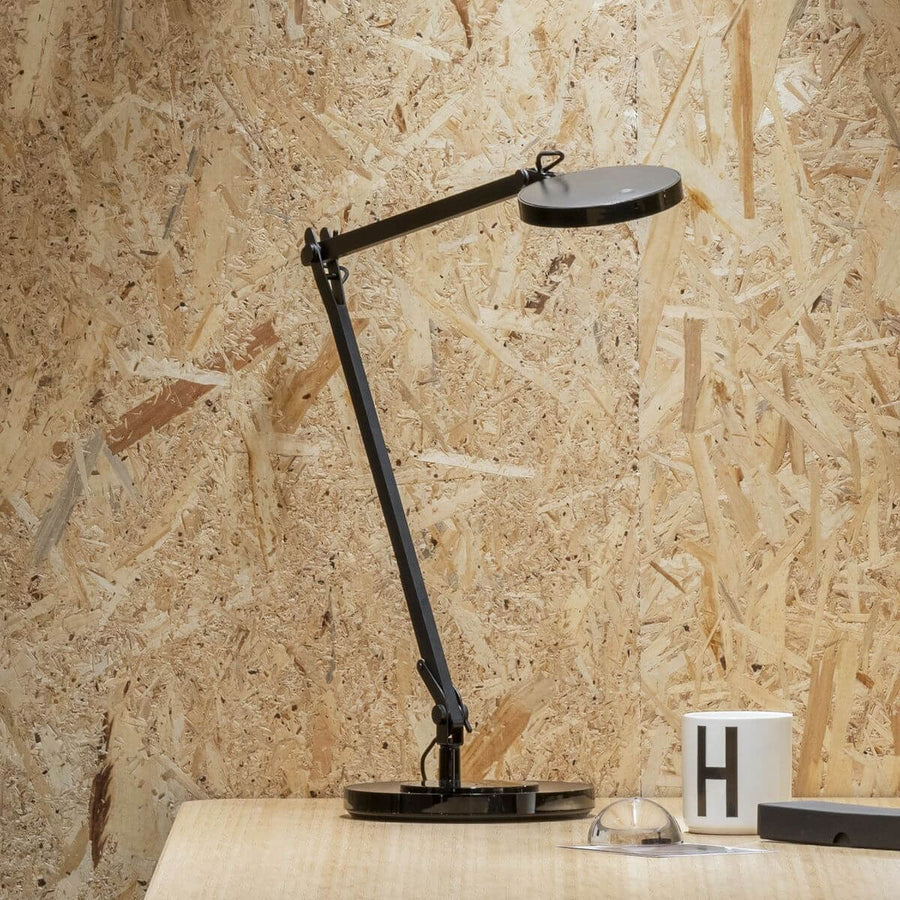 Lampe de bureau noire sur table en bois devant un mur en panneaux OSB