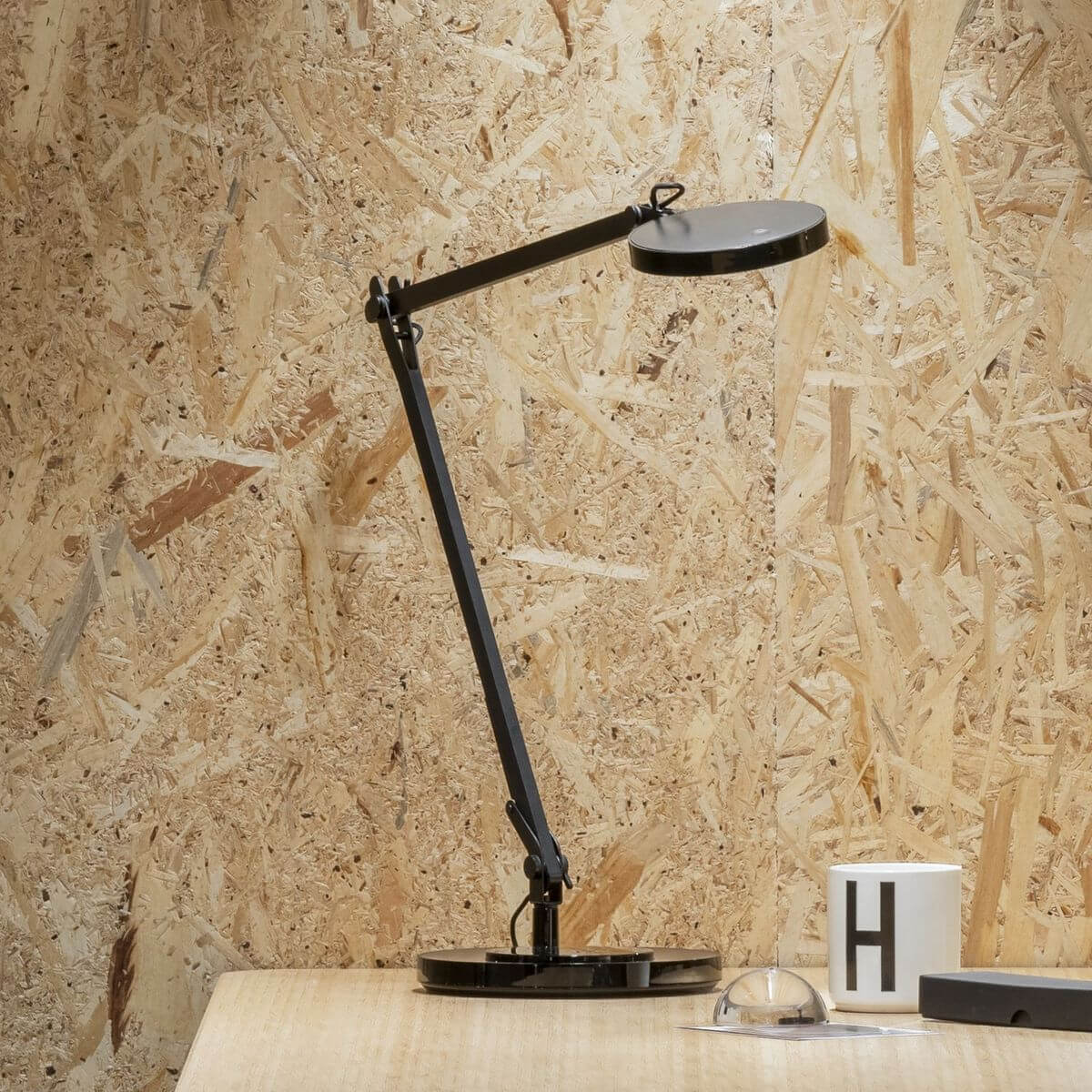 Lampe de bureau noire sur table en bois devant un mur en panneaux OSB
